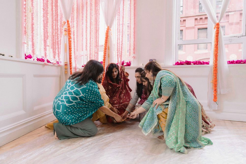 Women in colorful saris participating in a traditional floor ceremony with pink decorations.