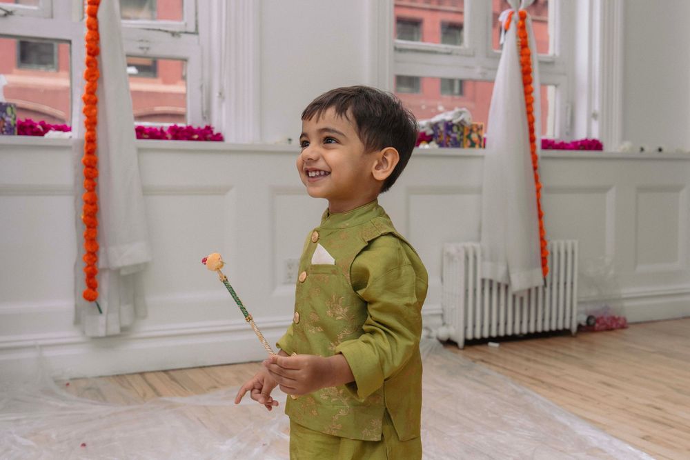 Child in olive green outfit playing and laughing in a bright indoor space.
