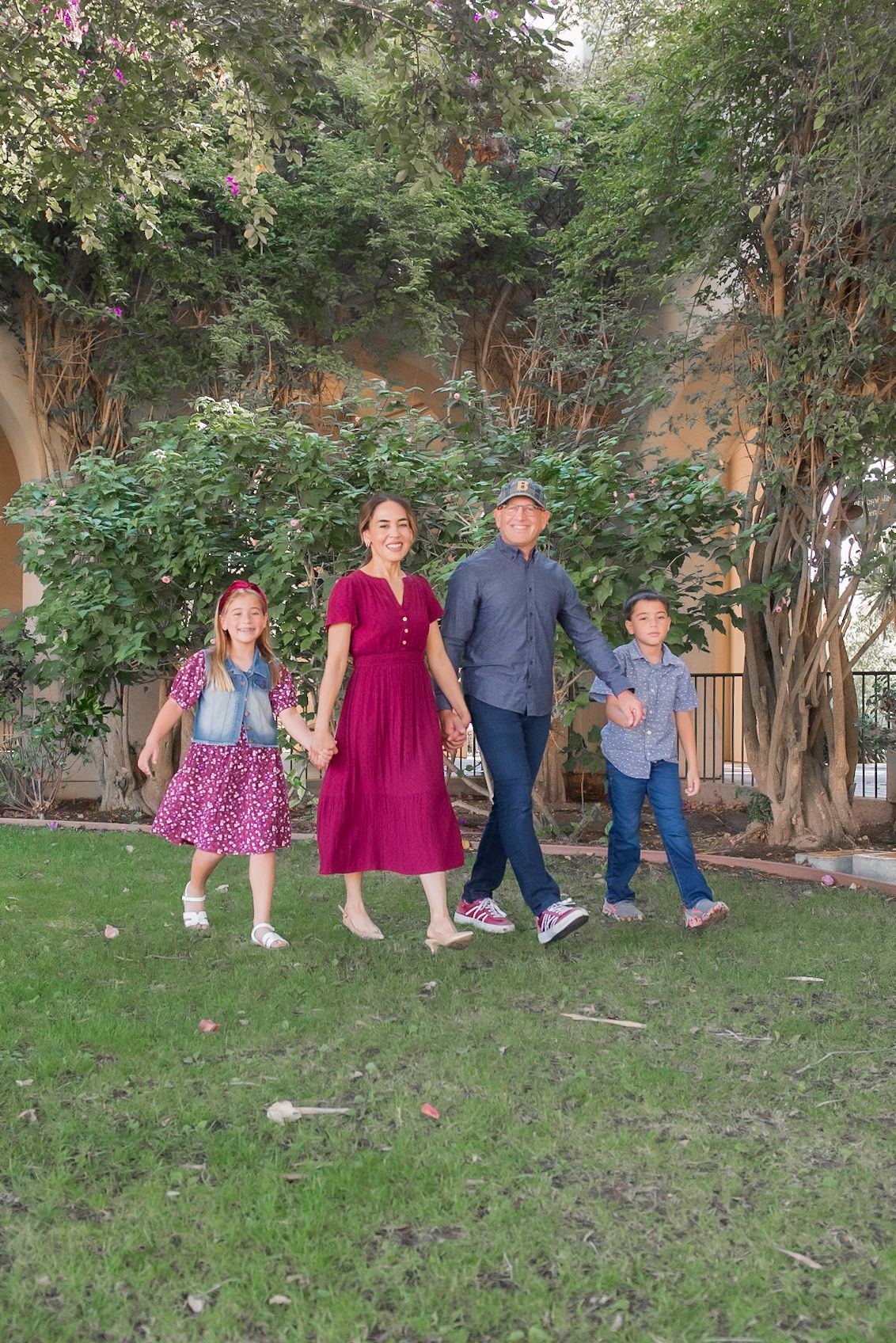 A group poses playfully on a grassy lawn near trees and bushes in coordinated outfits.