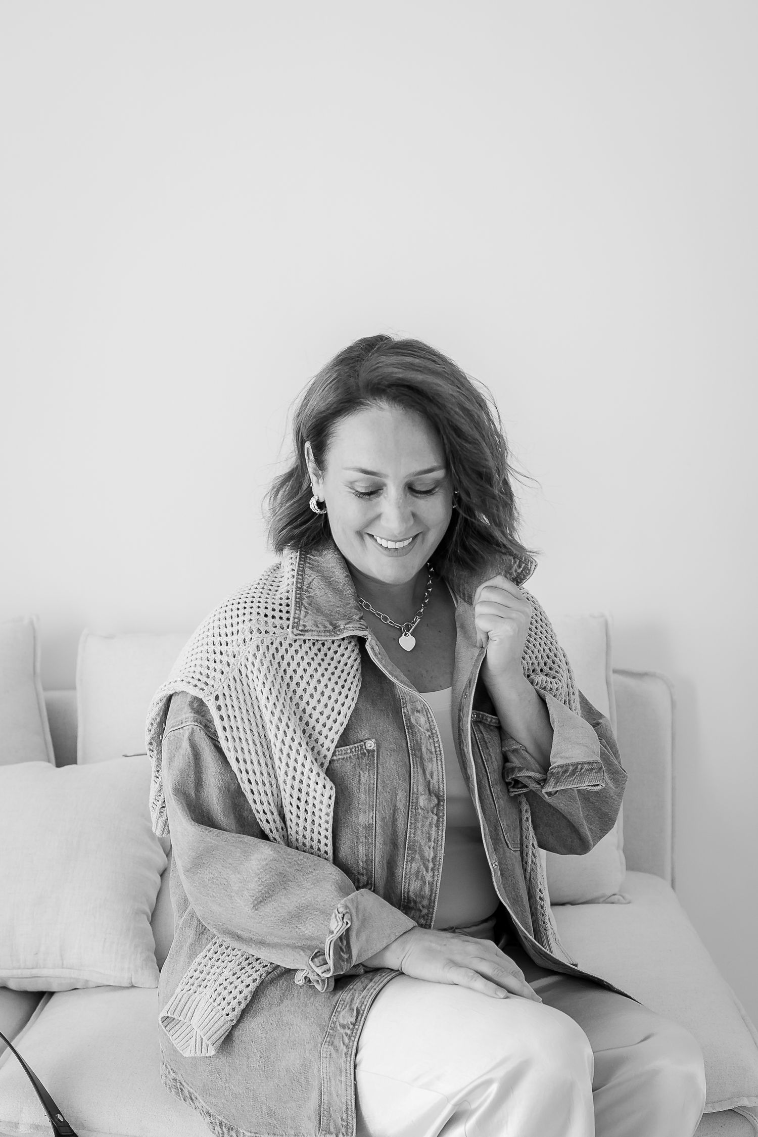 A woman in a polka dot shirt laughs joyfully while sitting on a white couch in a black and white photograph.