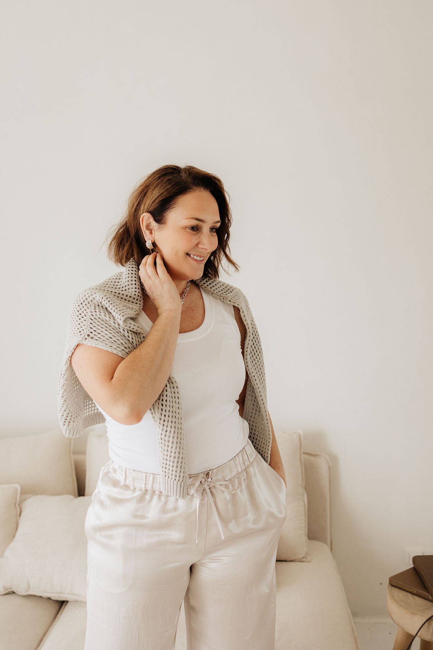 Woman in polka dot top lounging playfully on white bedding in bright minimalist bedroom setting.