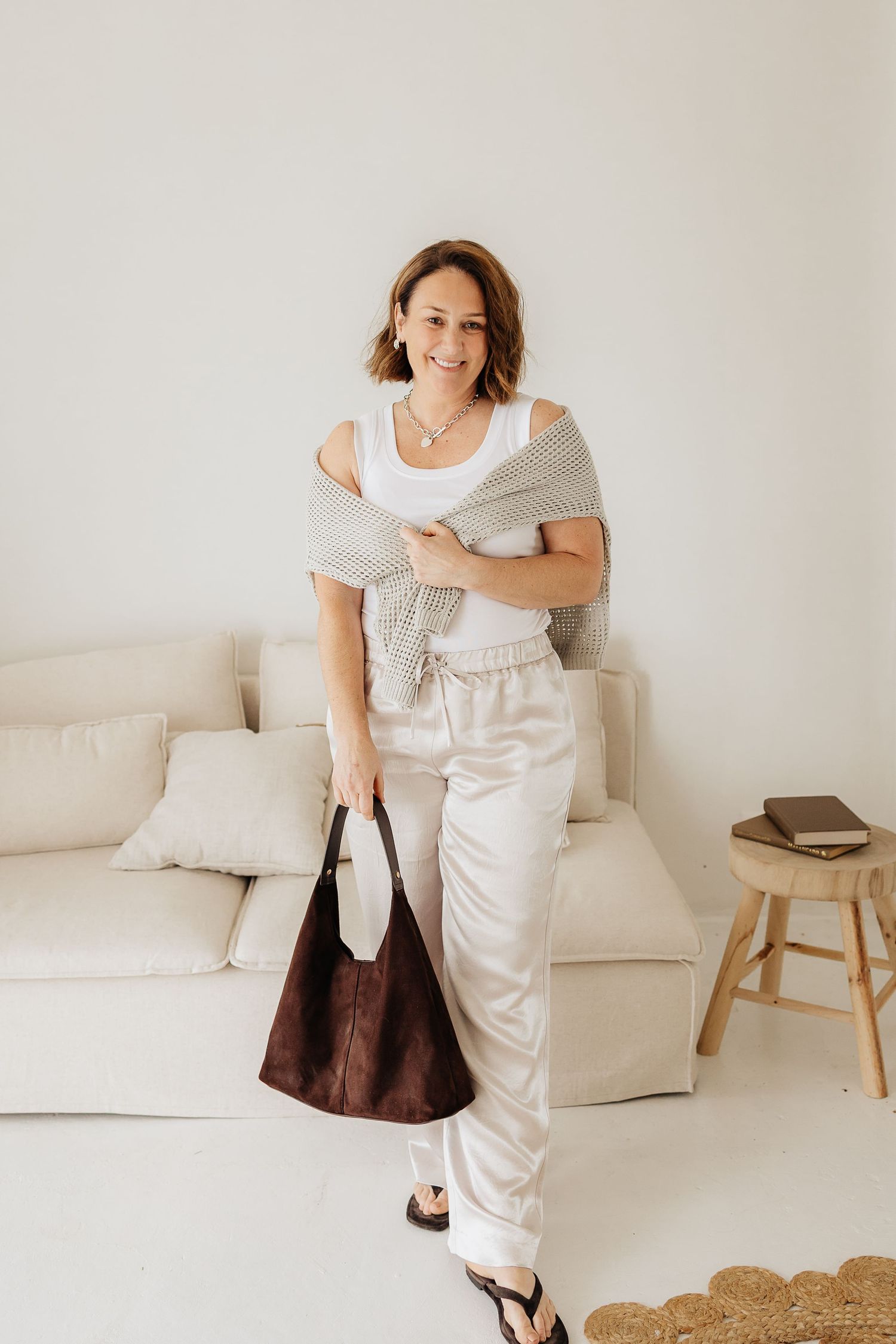 A fashion photoshoot against a white wall featuring casual loungewear styling with a white tank top and light pants.