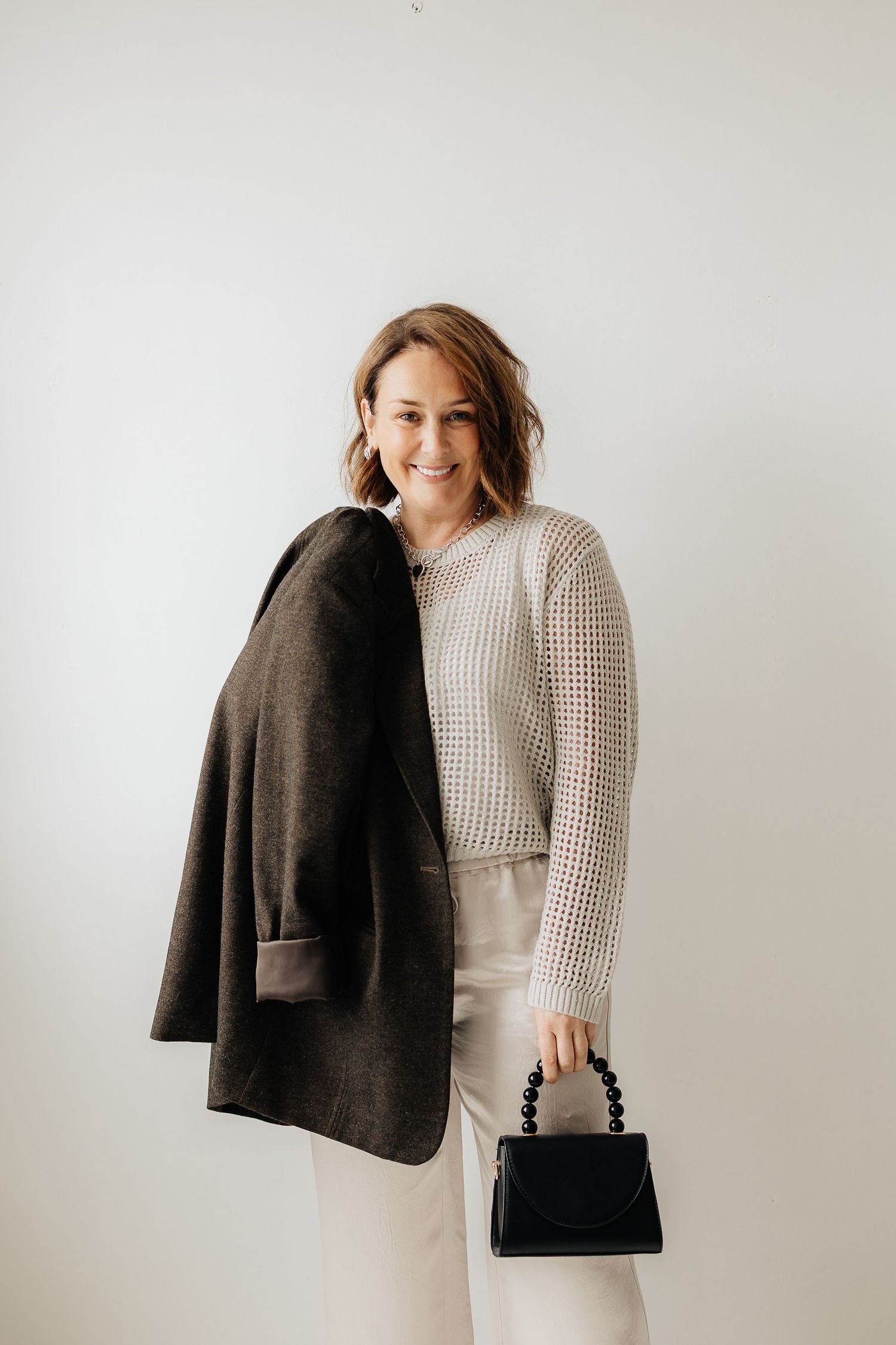 Minimalist fashion styling with a textured sweater, dark blazer and structured handbag against a white backdrop.