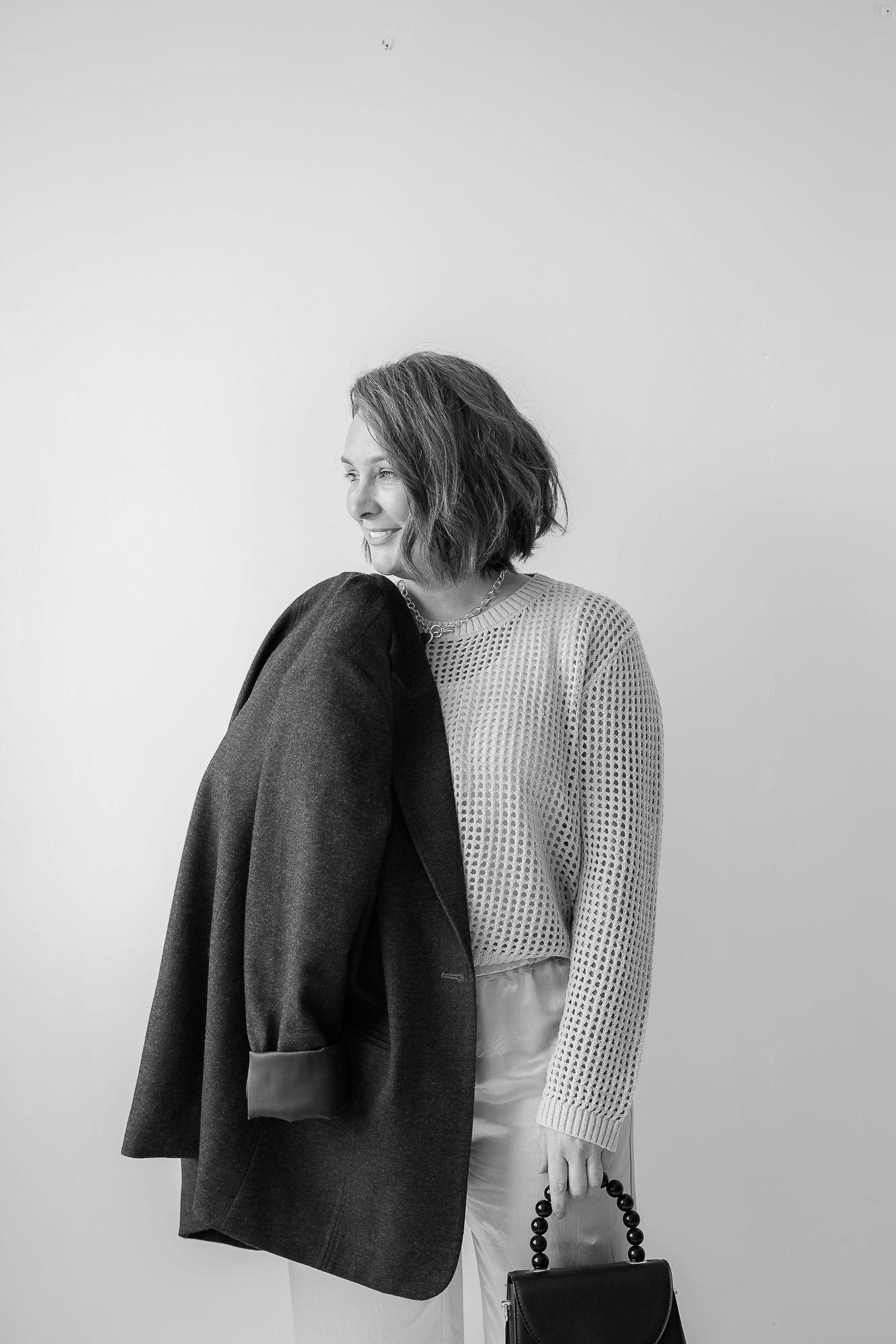 Black and white portrait of someone in a textured sweater holding a dark coat and handbag.