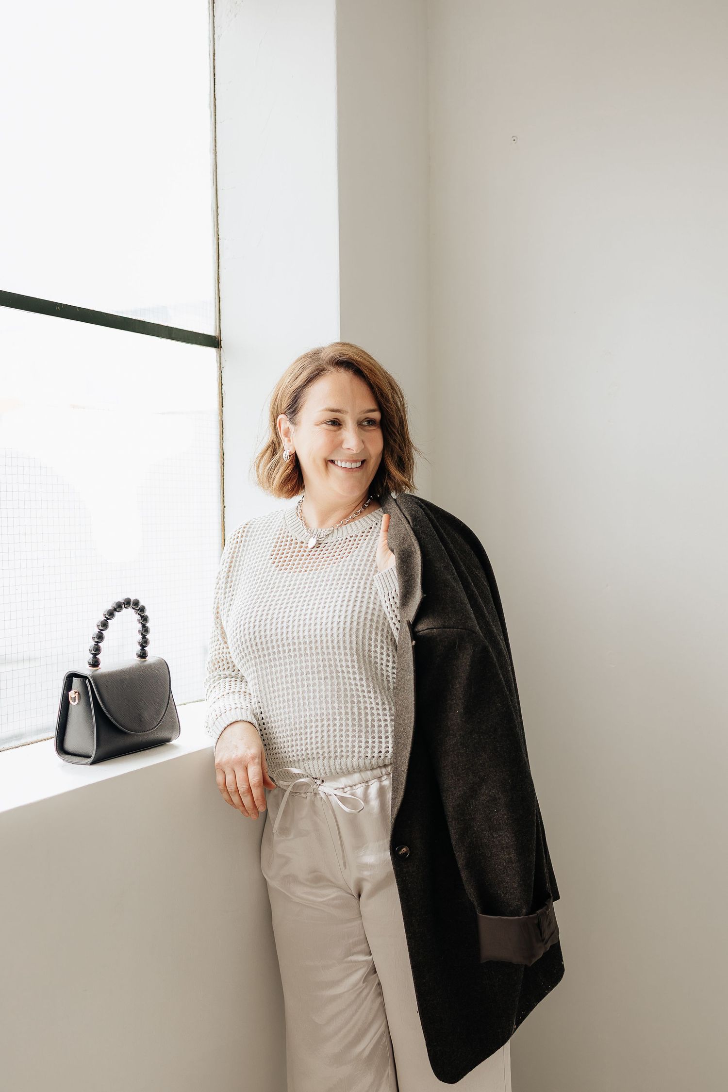 Stylish casual look with a black blazer, checkered top and light colored pants against a white wall.