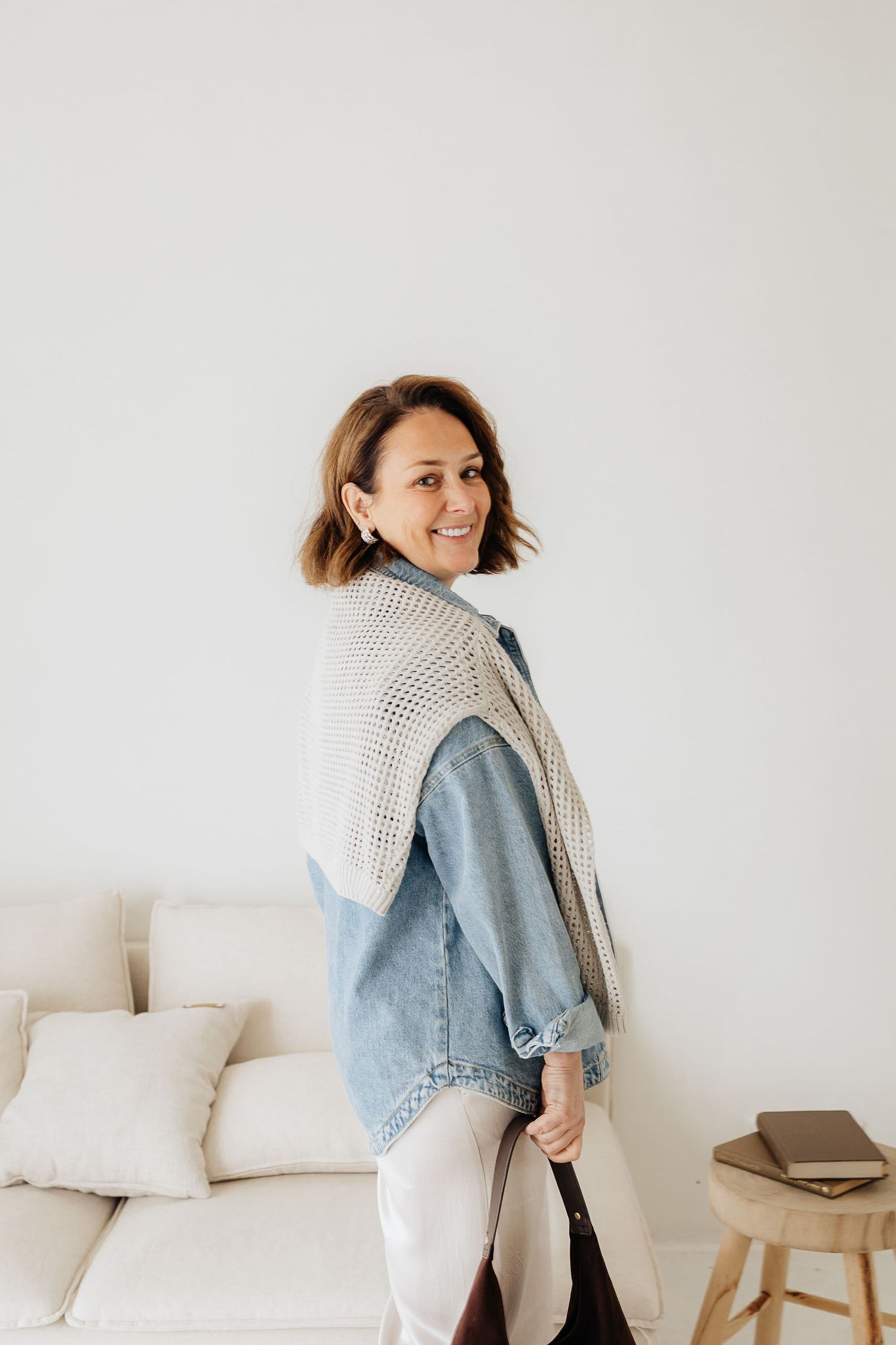 A casual outfit featuring a denim jacket layered over a cozy knit sweater in a bright minimalist interior setting.