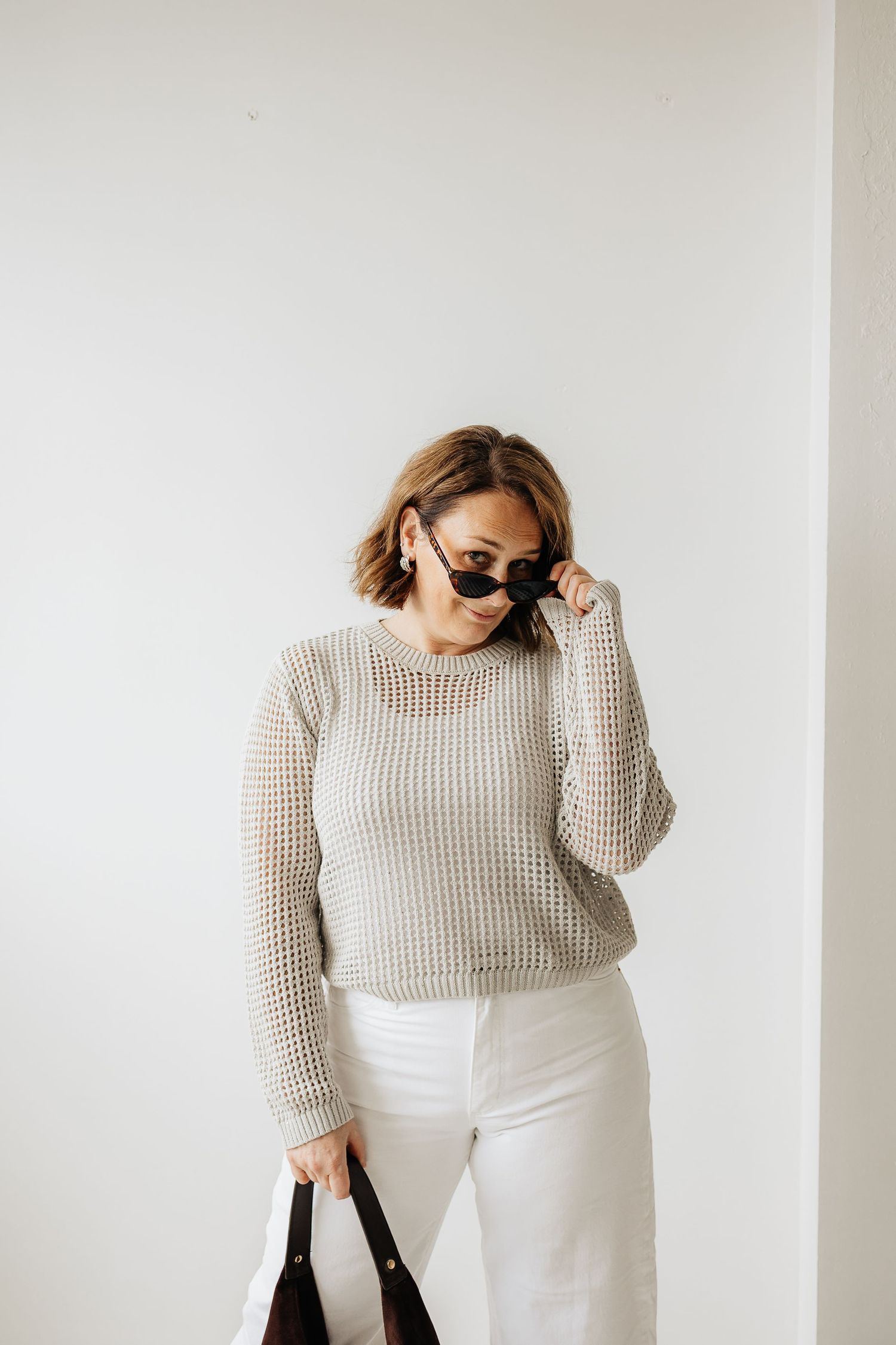 Model styled in cream knit sweater and white pants demonstrates minimalist fashion poses against neutral backdrop.