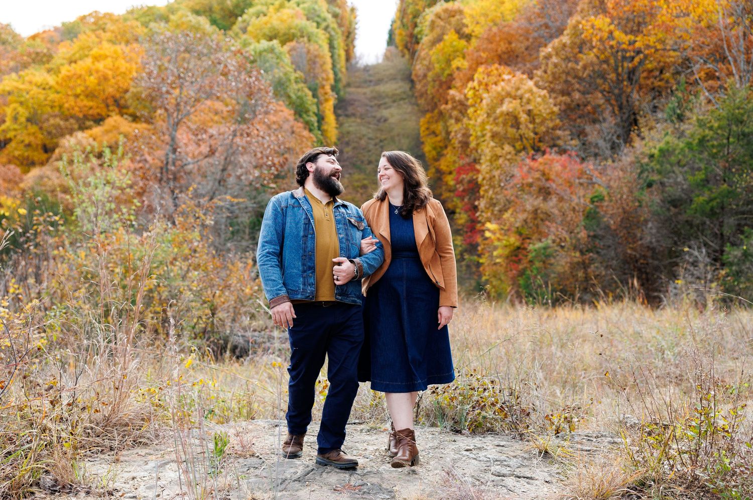 A couple enjoys a romantic autumn day outdoors surrounded by colorful fall foliage near a lake.