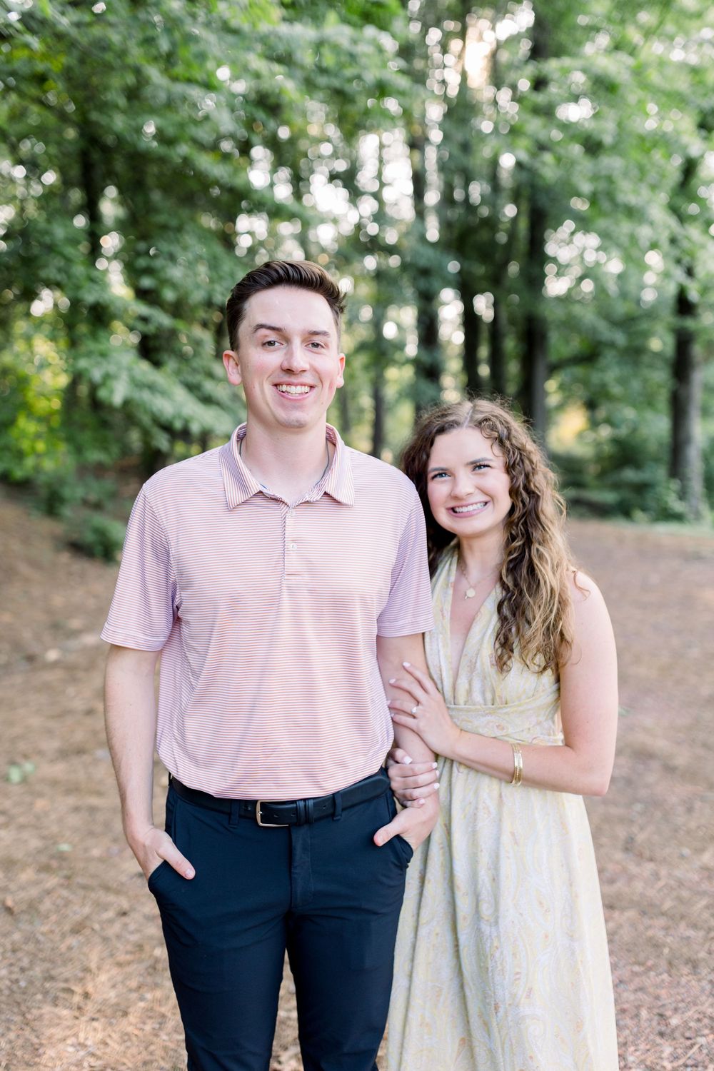 Couple in coordinated outfits sharing sweet moments in a sunlit wooded area.