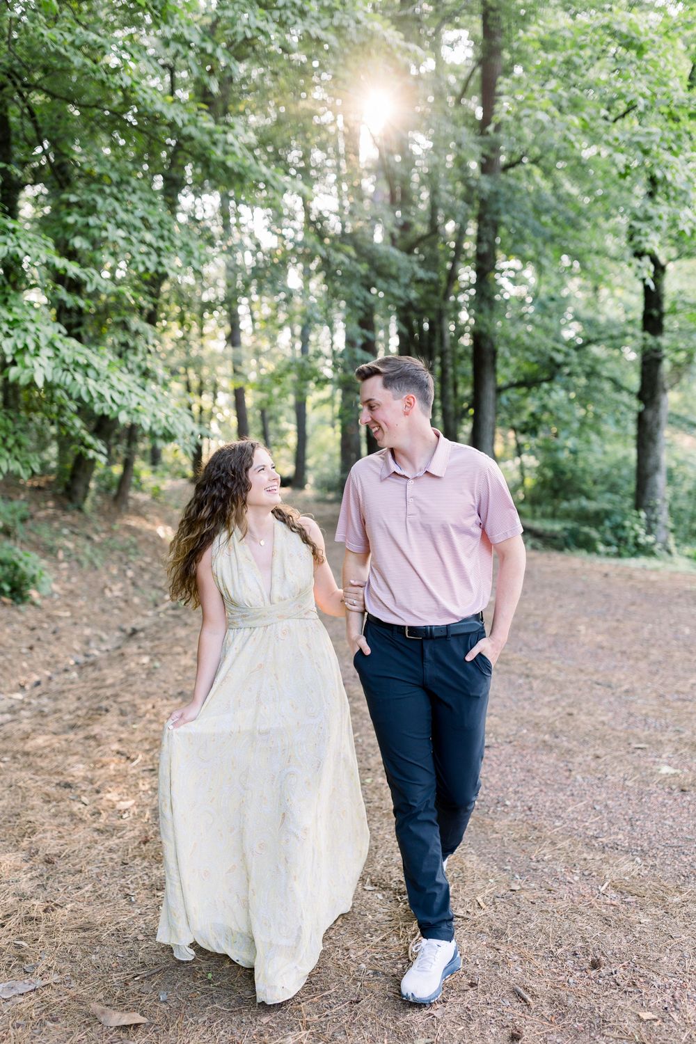 Couple walking together on a forest path with sunlight streaming through the trees.