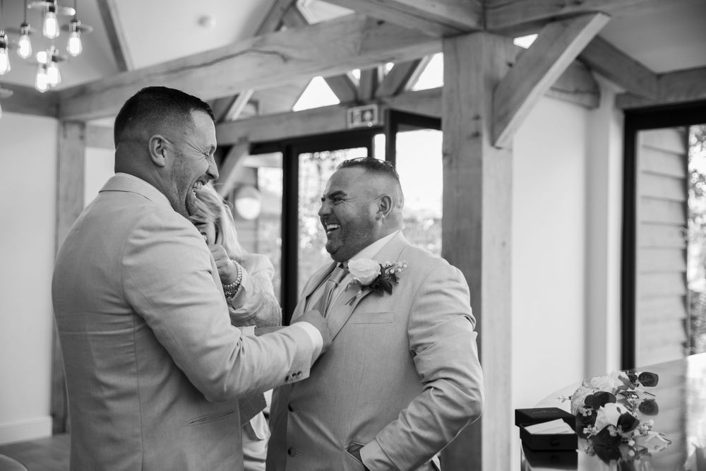 Two men in light gray suits share a joyful moment together during a wedding celebration.