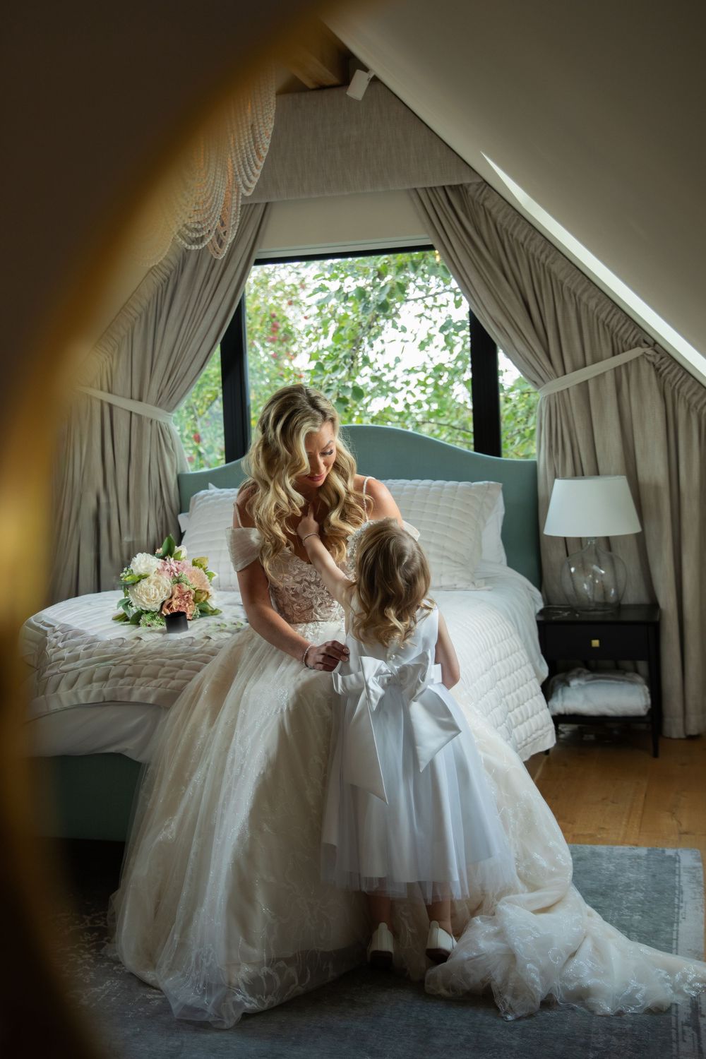 A tender moment captured in a sunlit room with flowing white wedding dresses and elegant curtains.