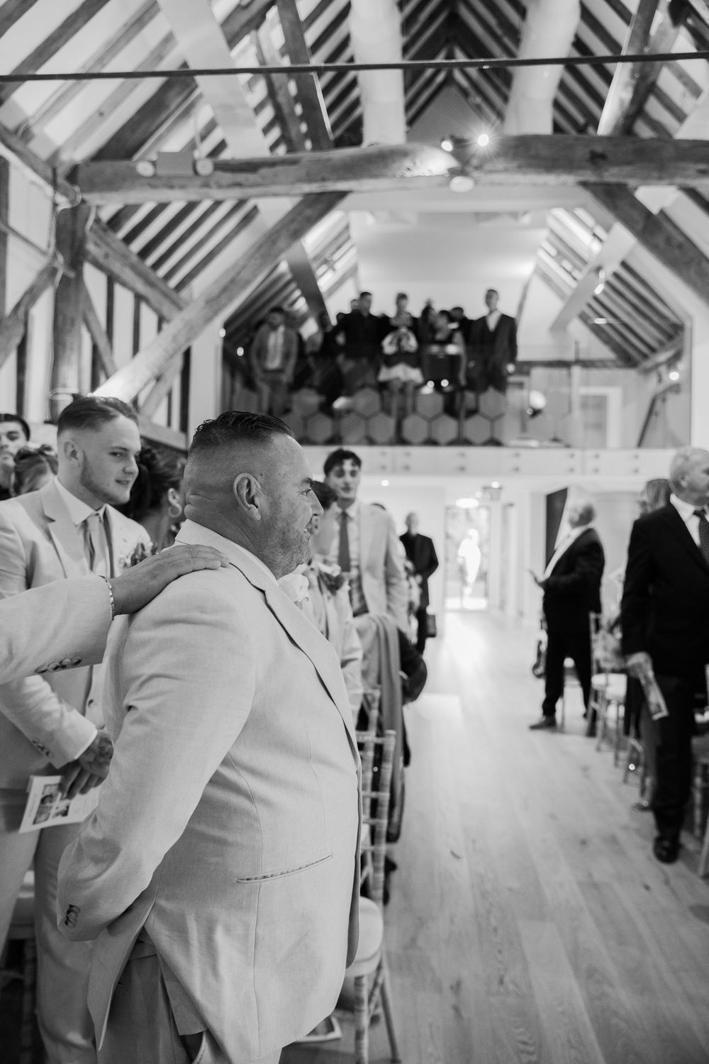 Wedding guests gather in a rustic barn venue with exposed wooden beams and natural lighting.