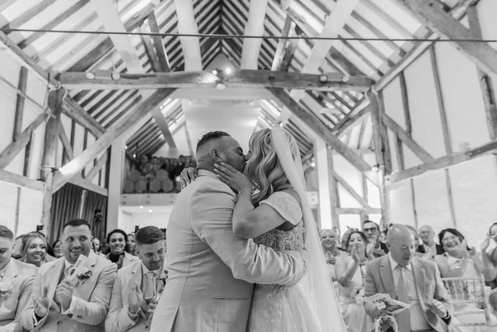 A couple shares their first kiss as newlyweds under a rustic wooden chapel ceiling.