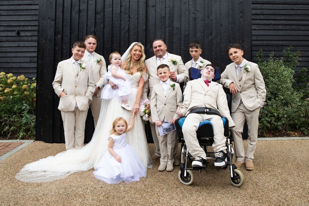 Wedding party in beige suits and white dresses pose together in an outdoor garden setting.