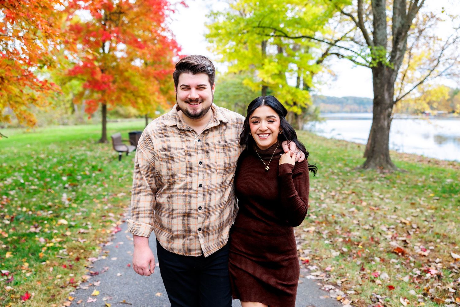 A couple enjoys a romantic autumn day outdoors surrounded by colorful fall foliage near a lake.