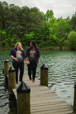 People walking on a wooden dock overlooking a serene lake surrounded by lush green trees.