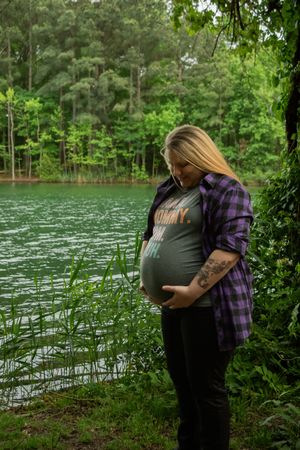 A couple shares an intimate moment by a serene lake surrounded by lush green trees and foliage.