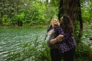 A person in a plaid shirt walks through lush green forest near a serene lake on a summer day.
