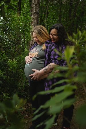 Two people embrace tenderly in a lush green forest setting, surrounded by vibrant foliage and dappled sunlight.