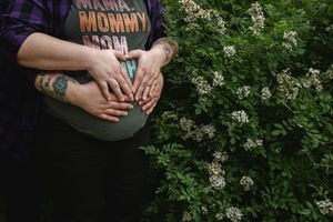 Hands wearing rings hold a bundle of white wildflowers against a green leafy background in natural lighting.