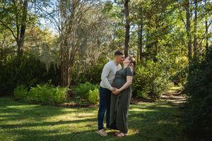 Couple embraces in a romantic outdoor photoshoot surrounded by lush green trees and natural sunlight.