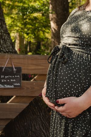 A polka dot maternity dress is shown against a natural outdoor setting with a wooden bench in the background.