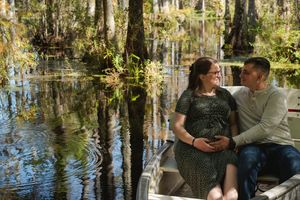 A couple sits together in a small boat on a scenic cypress swamp with reflective water and dappled sunlight.