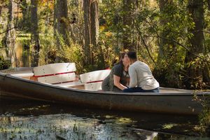 A couple paddling a wooden canoe through calm waters surrounded by autumn trees in a tranquil forest setting.