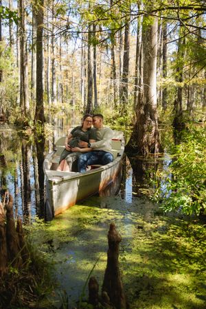 Kayakers explore a serene cypress swamp with dappled sunlight filtering through the trees onto the still waters.