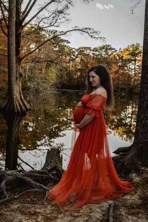 A red flowing gown creates ethereal movement by a serene lake with cypress trees at sunset.