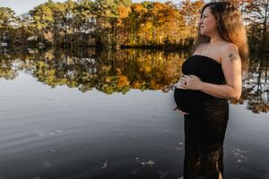 A couple embraces at sunset by a tranquil lake surrounded by autumn trees with golden foliage reflecting on the water.