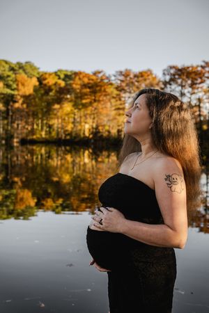 A serene autumn photoshoot by a lake with golden trees reflecting in still waters during sunset.
