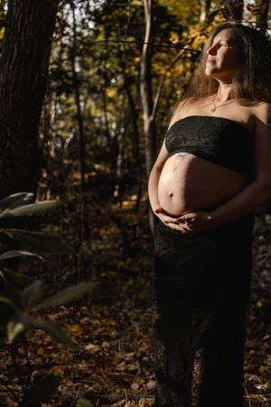 Artistic maternity photos captured in a wooded setting with dramatic lighting and shadows.