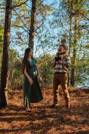 A couple poses together on a wooded hillside covered in fallen pine needles during golden hour.