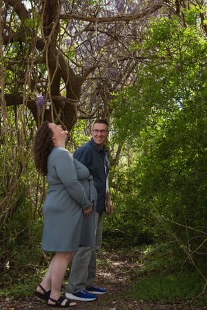 A couple shares a tender moment under blooming wisteria in a lush garden setting.