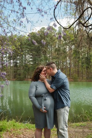 A romantic moment between a couple by a serene lake with wisteria flowers hanging overhead.