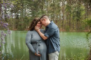 A romantic couple embraces in front of a serene lake surrounded by pine trees on a misty afternoon.