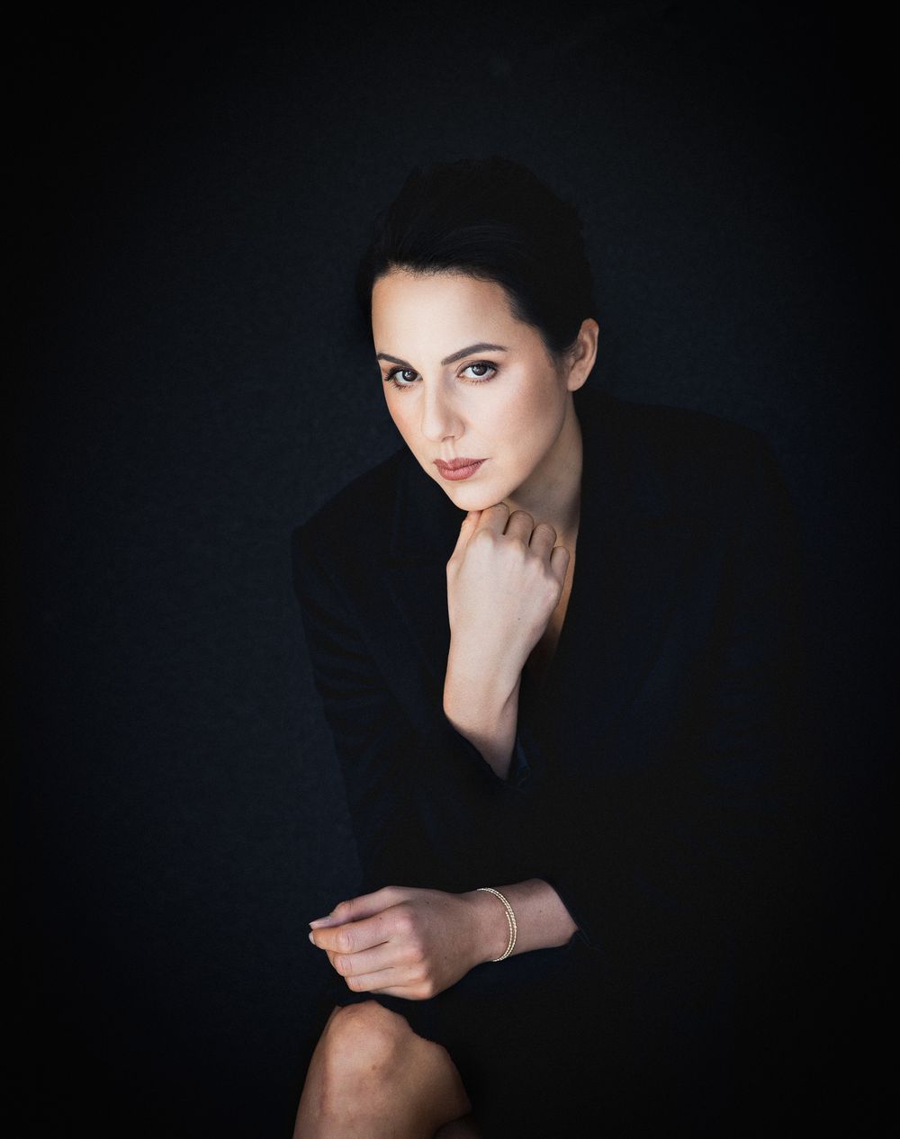 Refined and elegant portrait of a woman framed by a black backdrop and soft light.