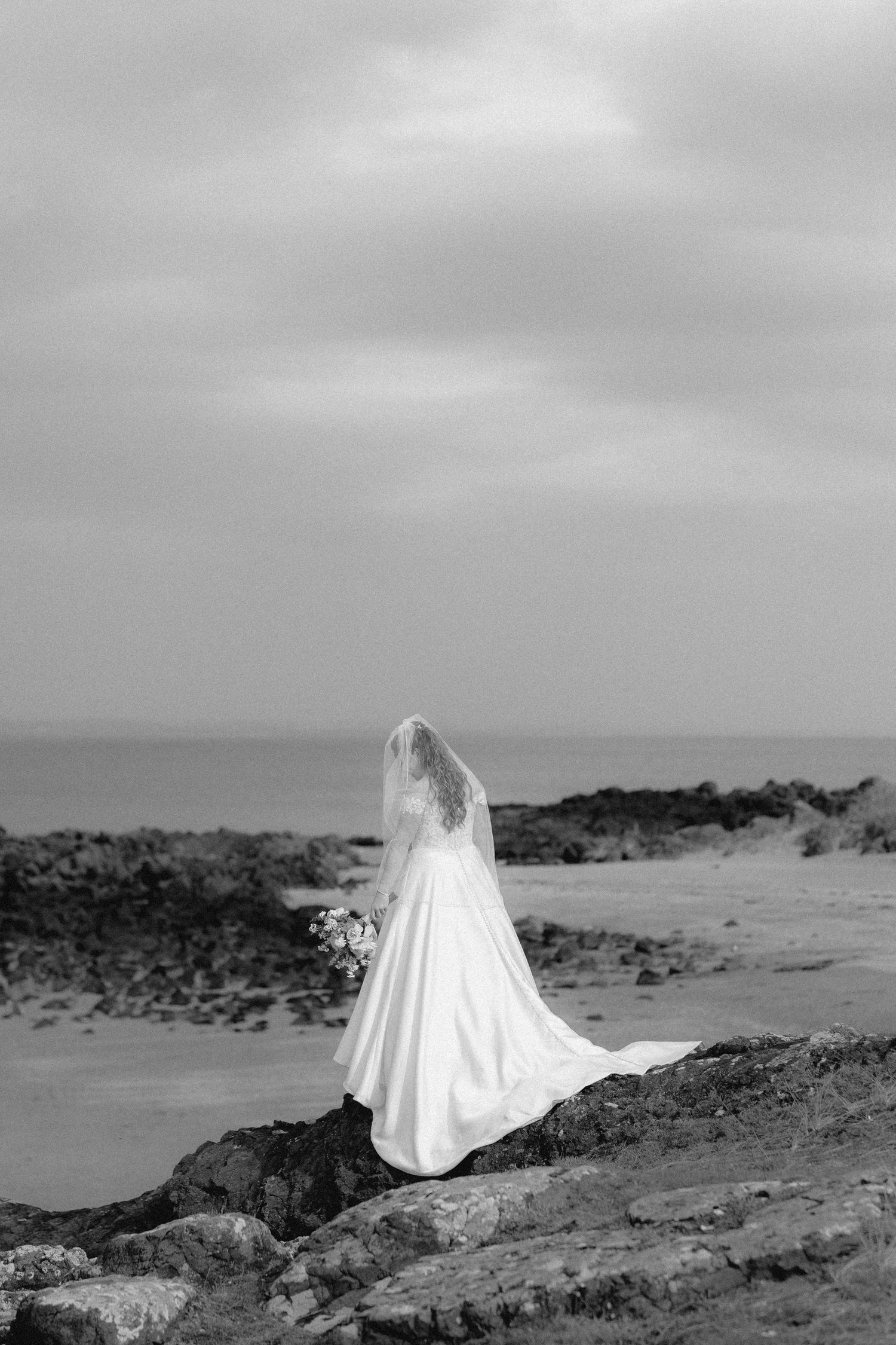 A ghostly figure in white cloth stands alone against a stark desert landscape in black and white.