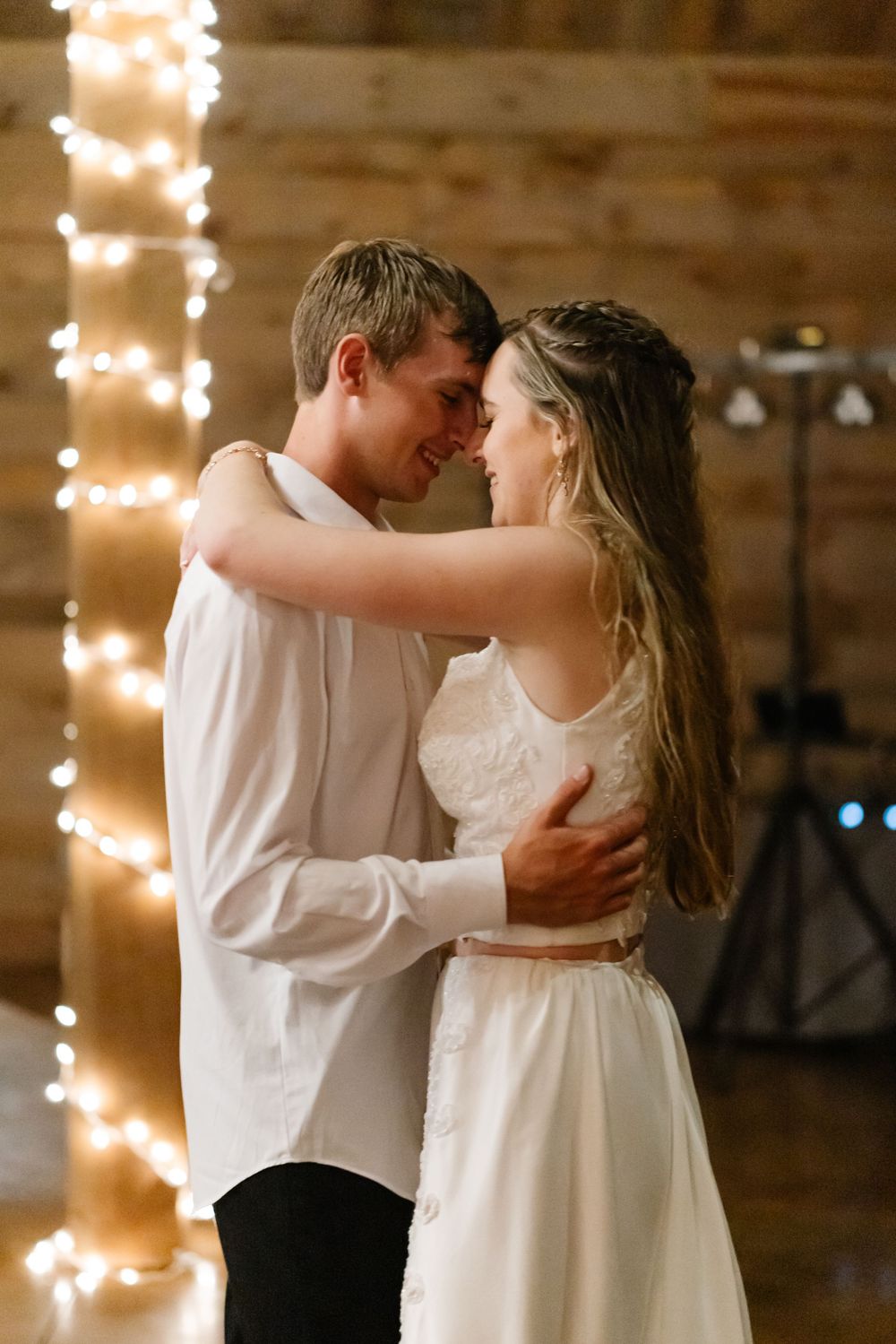 Romantic first dance between newlyweds under warm string lights in rustic venue.