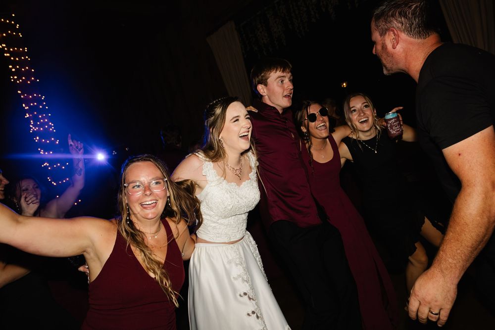 Wedding guests dancing and celebrating at reception with blue lighting effects.