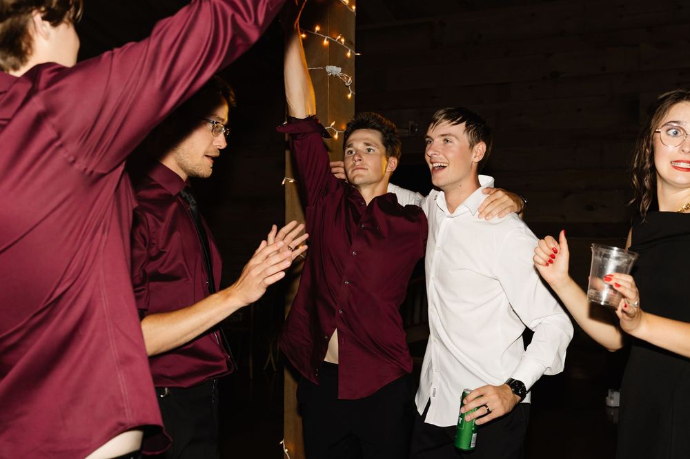Wedding party in burgundy attire dancing enthusiastically at reception.