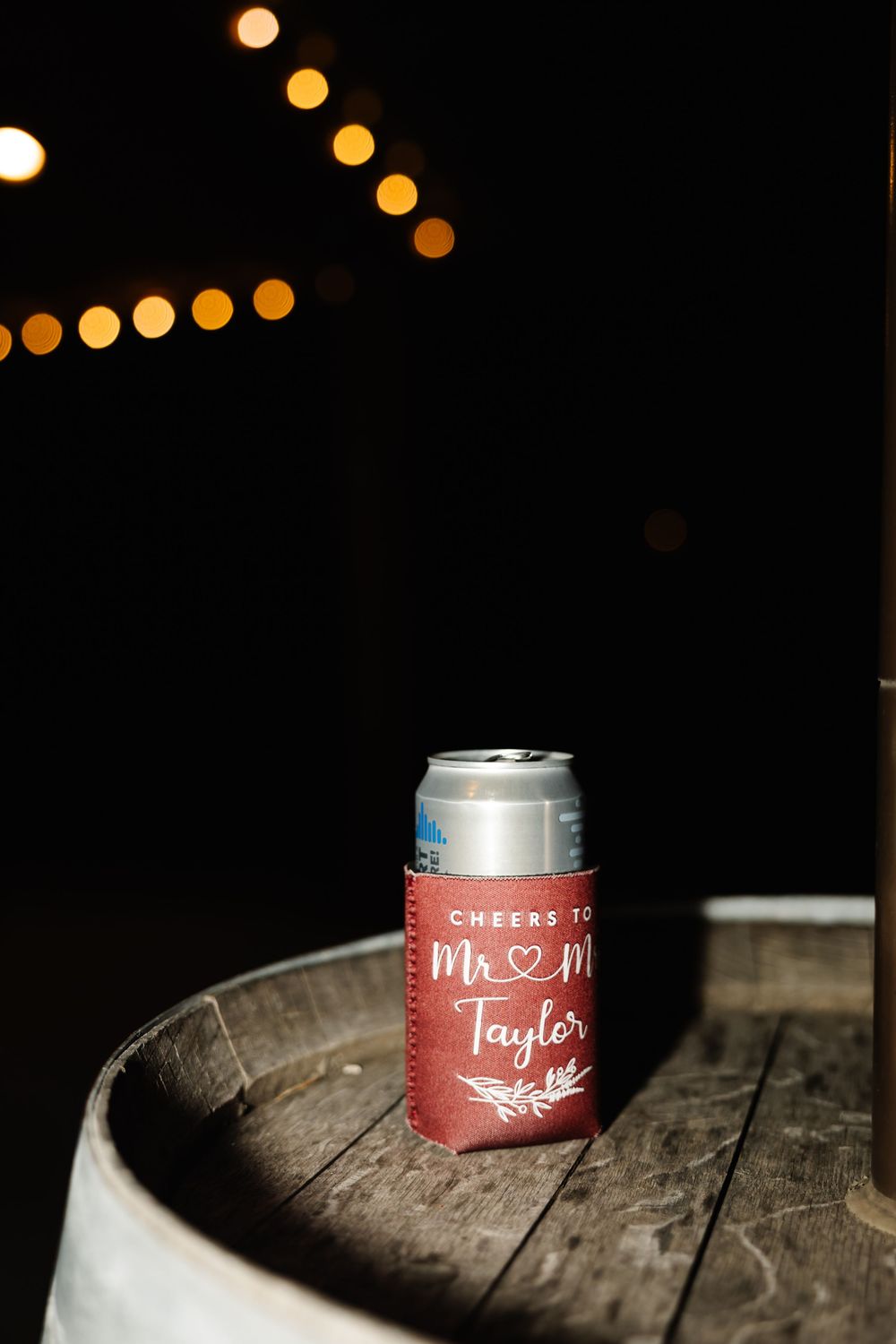 Personalized wedding drink koozies on wooden surface with string lights in background.