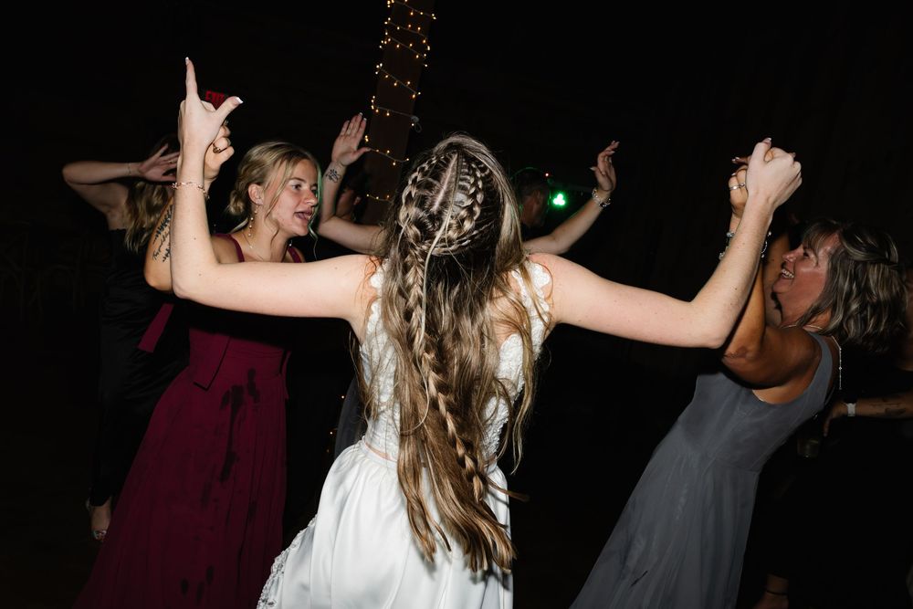 People dancing and celebrating on a dark dance floor with festive lighting in the background.
