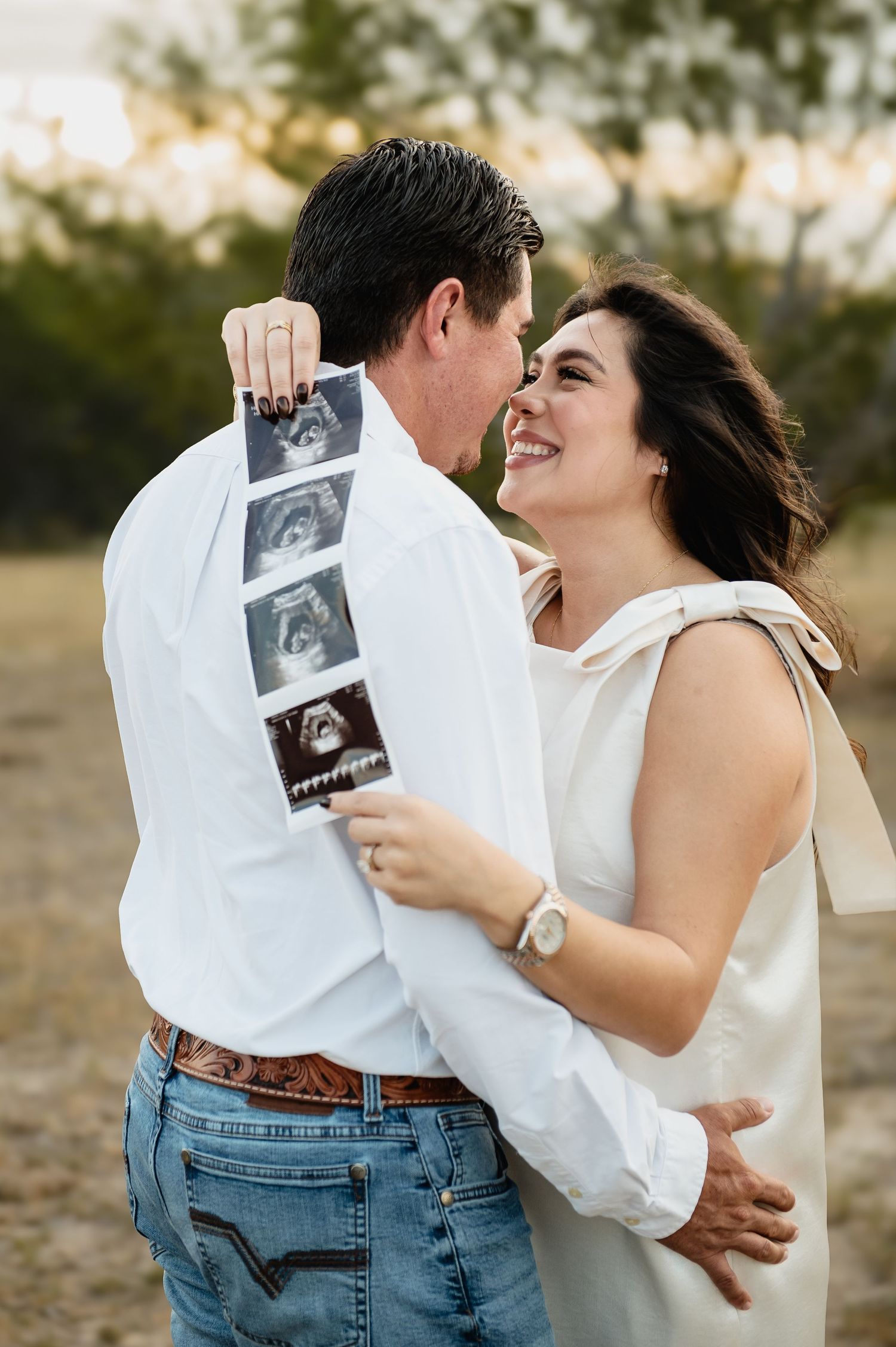 A couple shares an intimate moment while holding ultrasound photos in a romantic outdoor photoshoot.