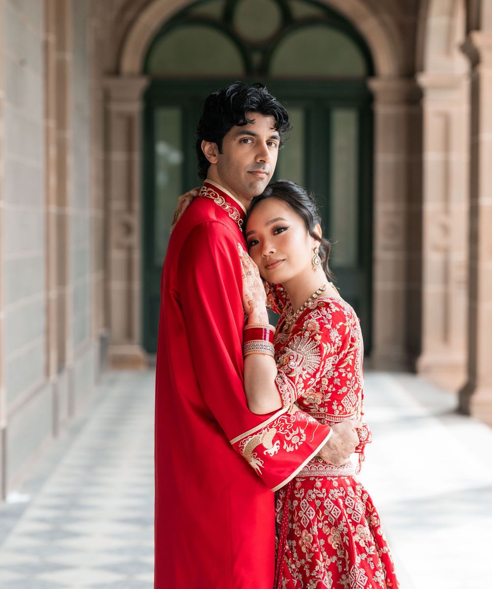 Couple in traditional red attire pose intimately in an elegant arched corridor for romantic wedding photos.