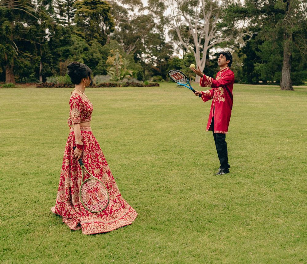 A couple in traditional Indian wedding attire poses in a scenic outdoor park setting with lush green grass.