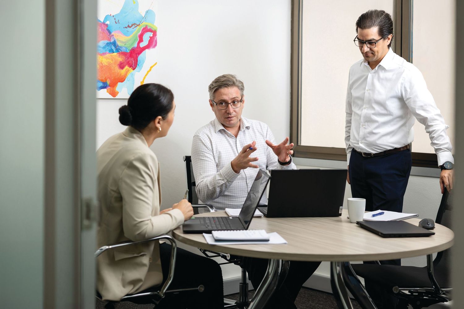 Business professionals collaborate during a meeting in a modern office conference room with colorful wall decorations.