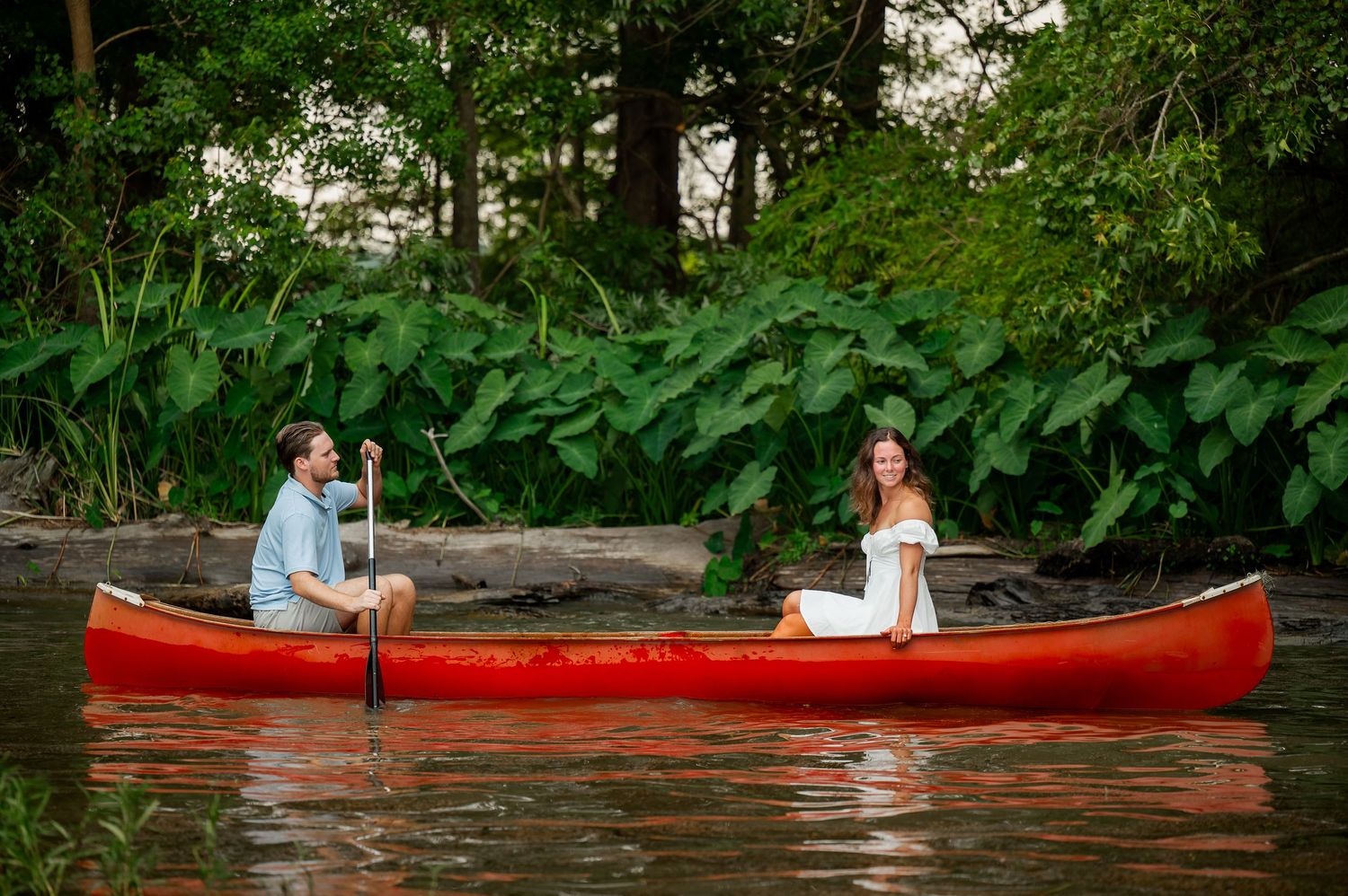 Couple paddling a bright red canoe down a peaceful river surrounded by greenery.